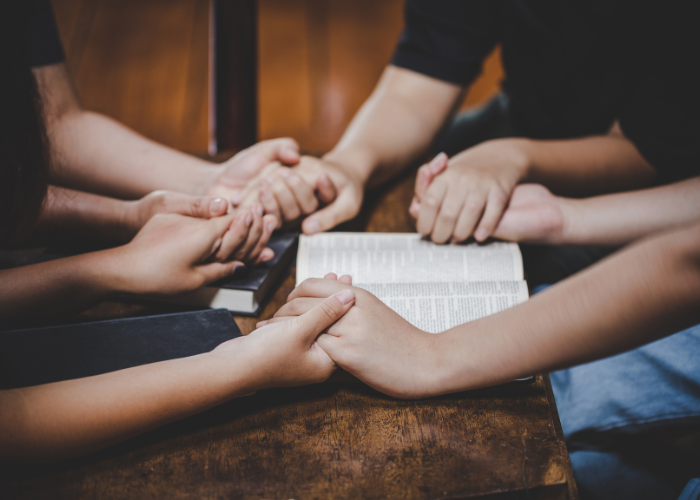 People holding hands praying over a Bible