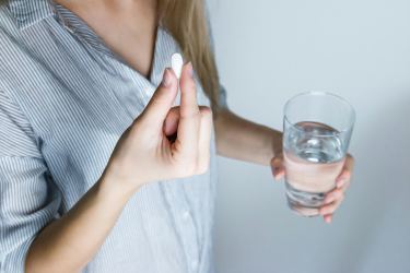 Woman taking a white pill with a glass of water