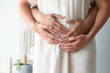 Husband hugging wife with their hands on her pregnant belly